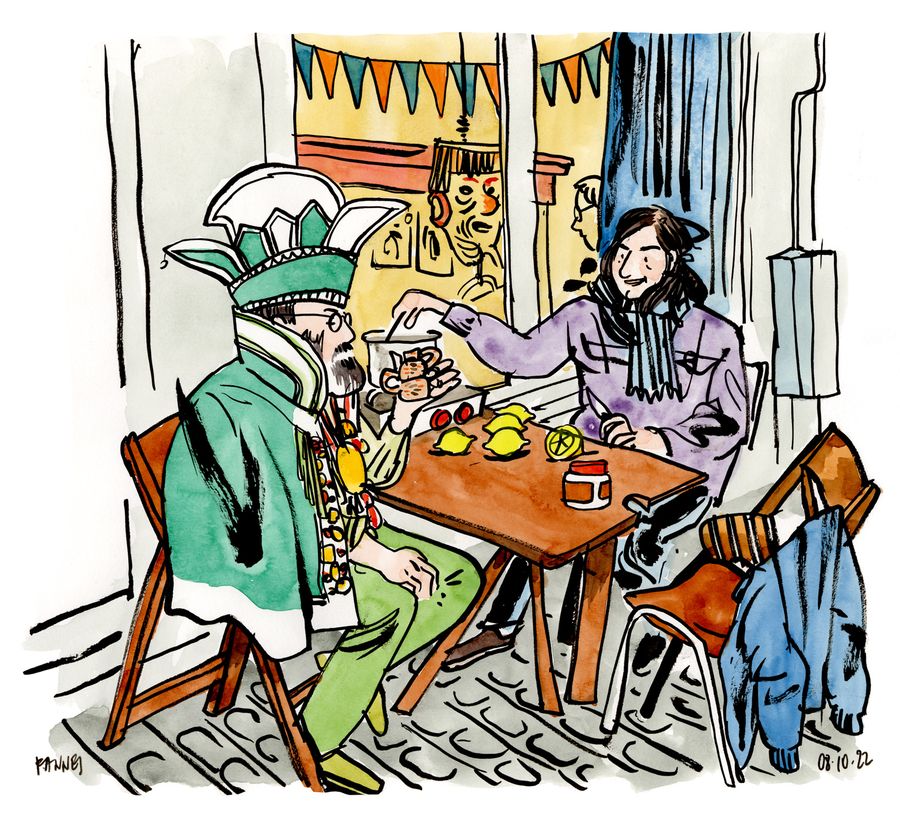 Two men at a café table, one in green ceremonial dress with a crowned hat
