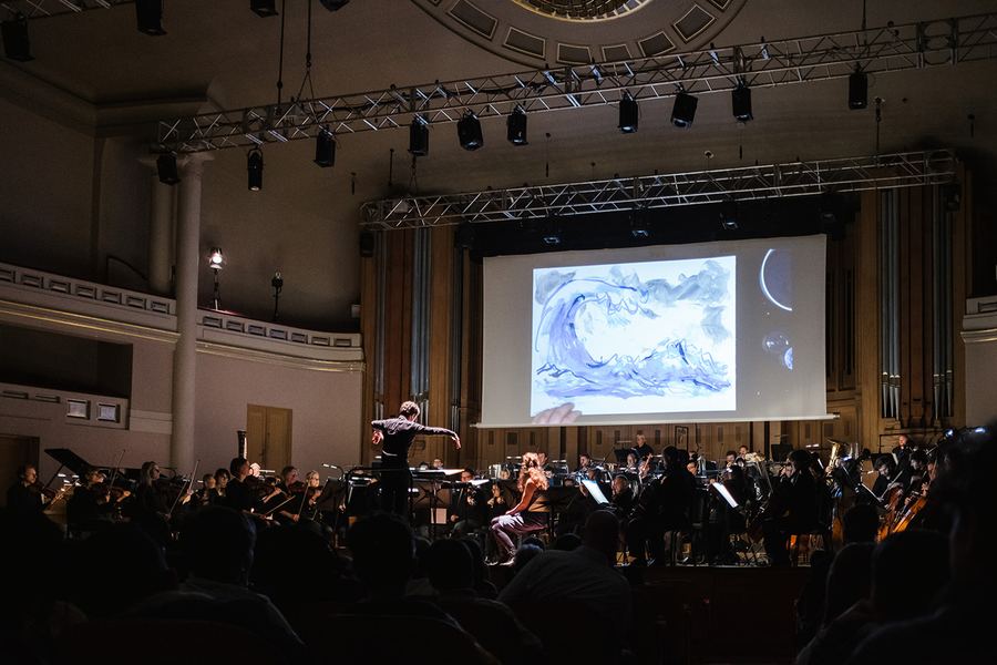 Concert photo: the full orchestra in the hall, a drawing of waves on the screen