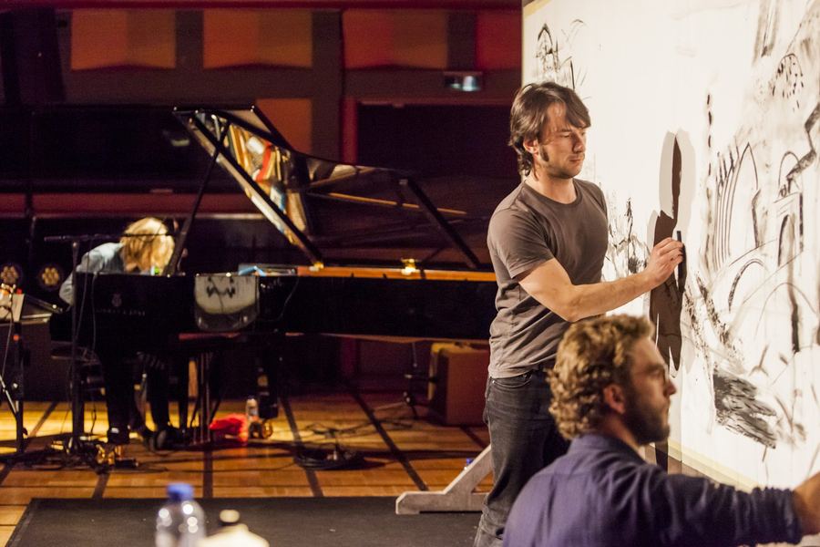 Stage photo: the artists drawing while the musician plays the grand piano