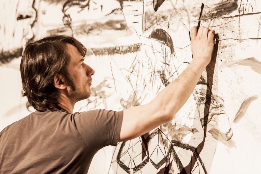 Stage photo: an artist reaches up to draw with a brush