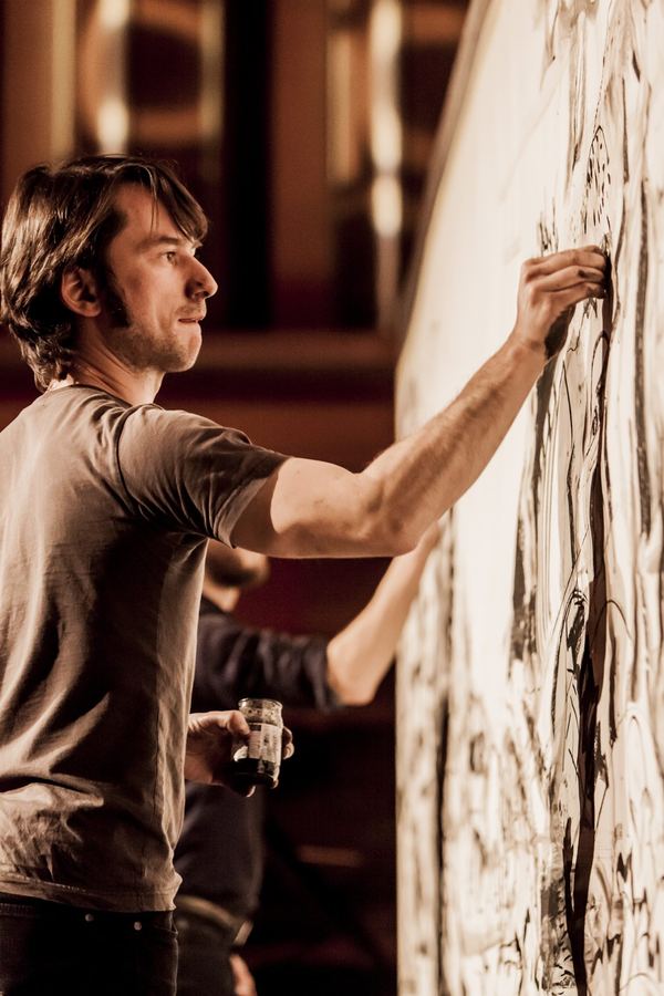 Stage photo: an artist drawing, a pot of ink in his other hand